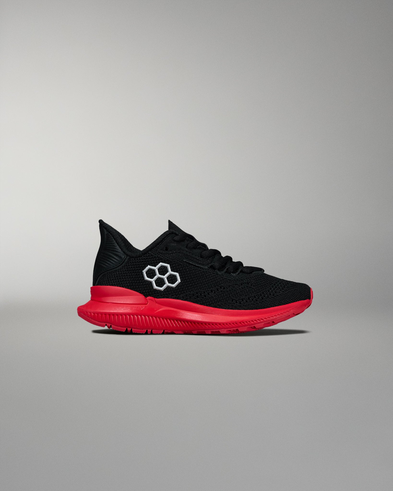 Side view of a black RUDIS training shoe featuring a red midsole and outsole with a white hexagon logo on the upper. Displayed on a neutral gray background.