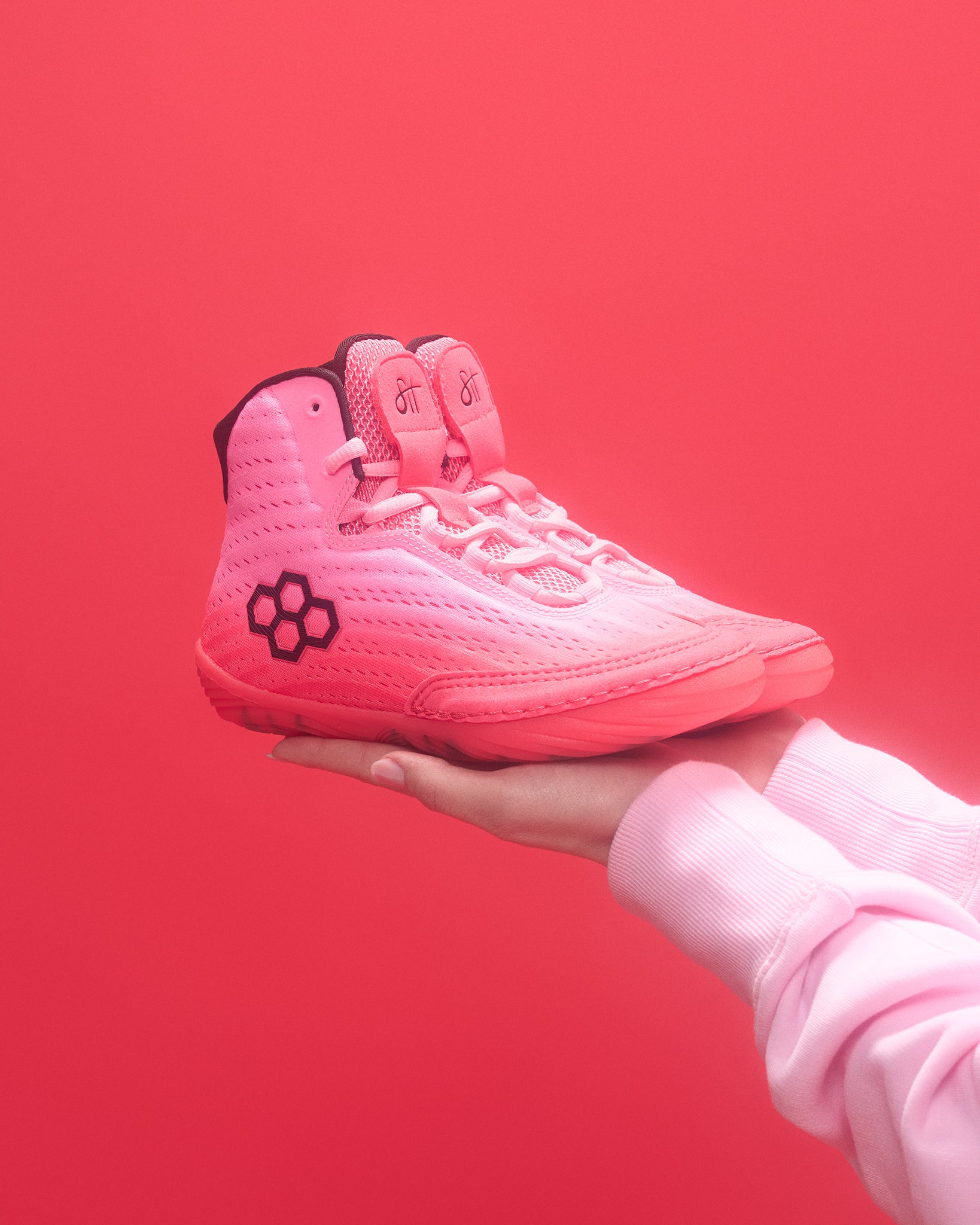 Pink wrestling shoe held in a hand against a red background