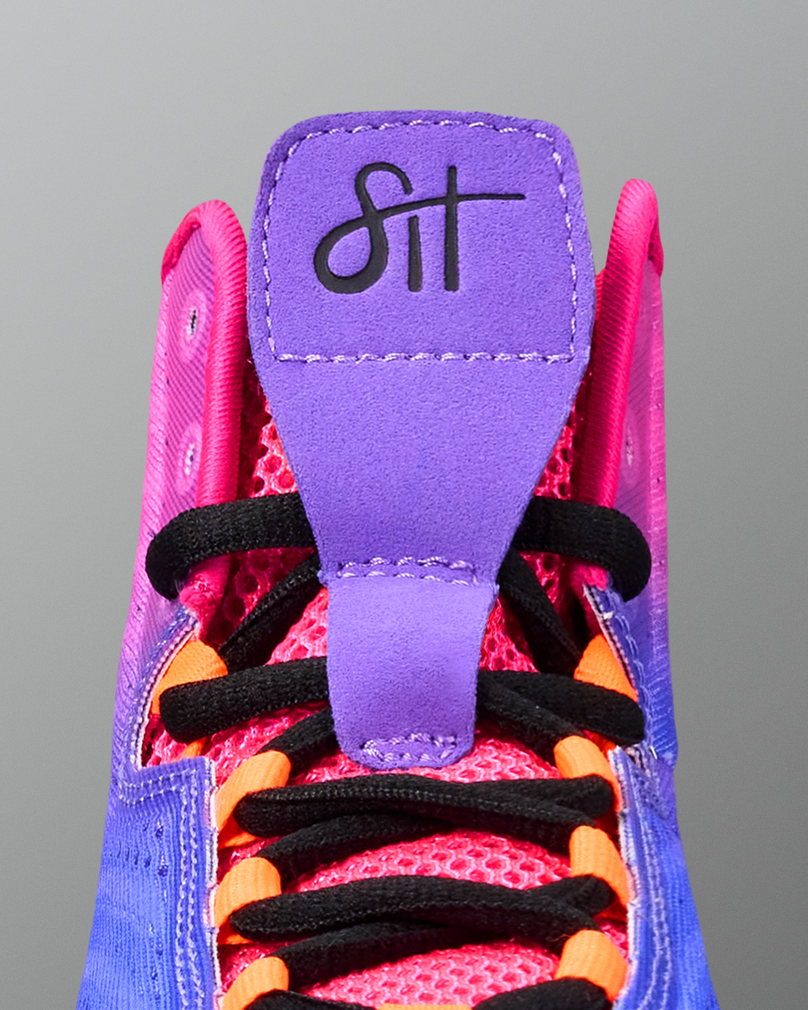 Close-up of a pink and purple wrestling shoe with black laces on a gray background
