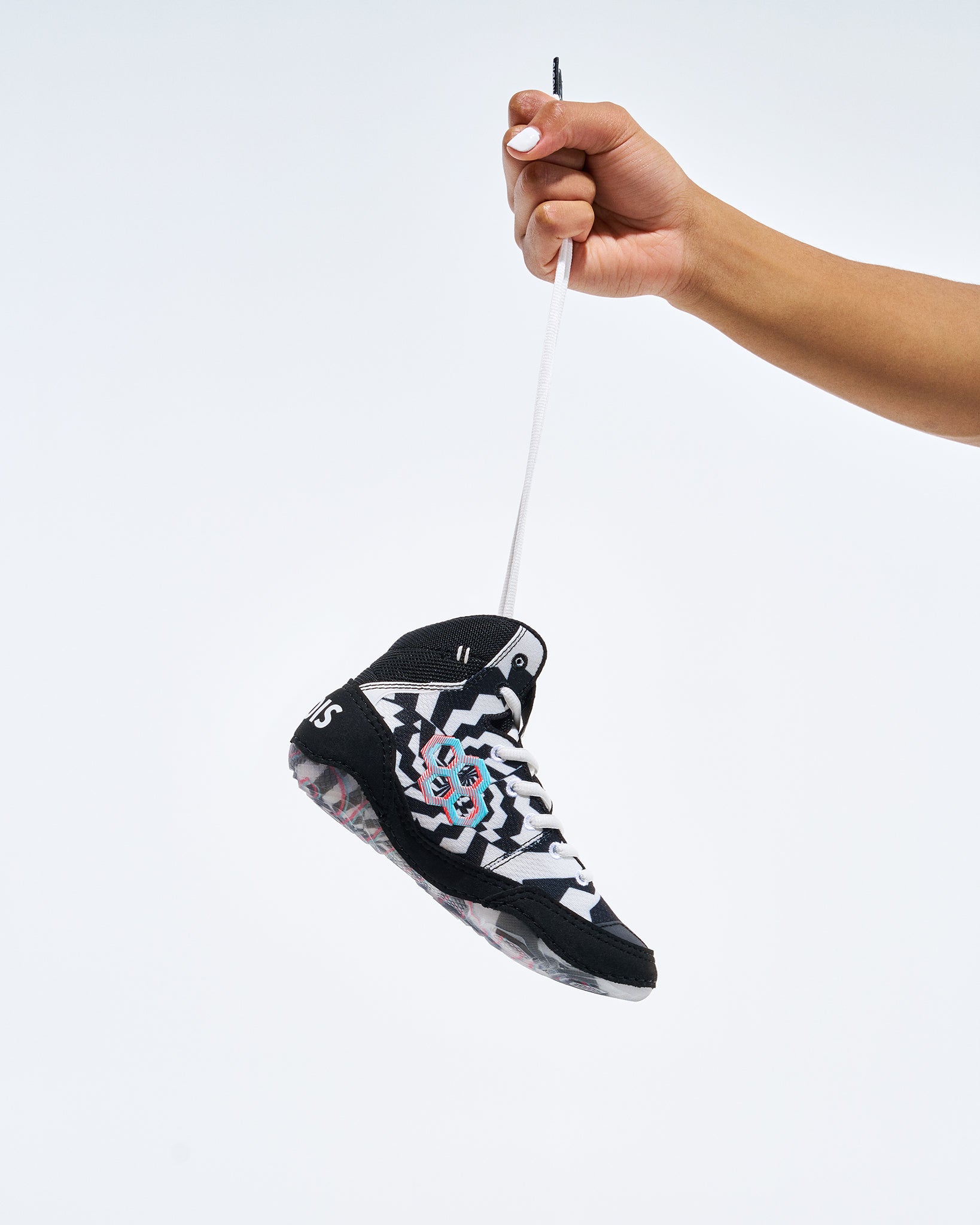 A miniature black, white, and gray wrestling shoe being held by a hand against a plain white background.