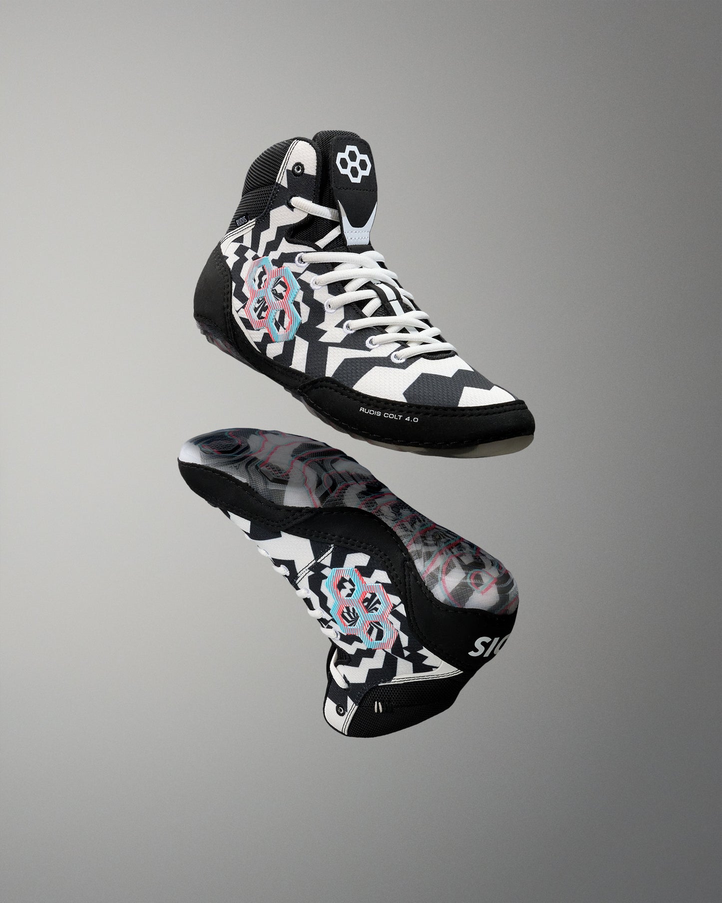 A pair of high-top wrestling shoes floating against a neutral gray gradient background. The shoes feature a black, white, and gray geometric pattern with a pink and blue circular graphic on the side and a white logo on the tongue.