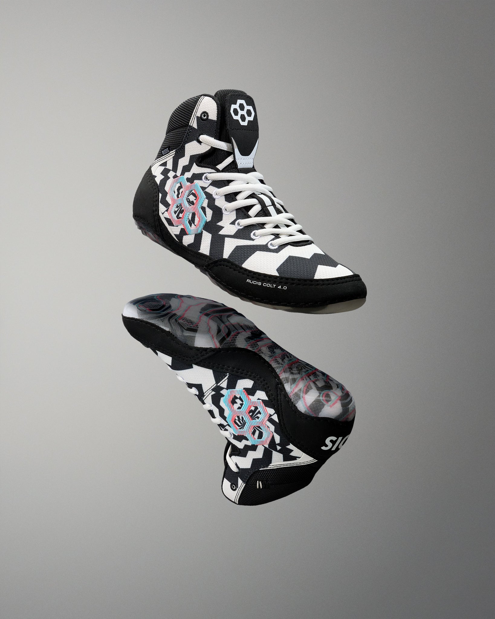 A pair of high-top wrestling shoes floating against a neutral gray gradient background. The shoes feature a black, white, and gray geometric pattern with a pink and blue circular graphic on the side and a white logo on the tongue.