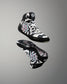 A pair of high-top wrestling shoes floating against a neutral gray gradient background. The shoes feature a black, white, and gray geometric pattern with a pink and blue circular graphic on the side and a white logo on the tongue.