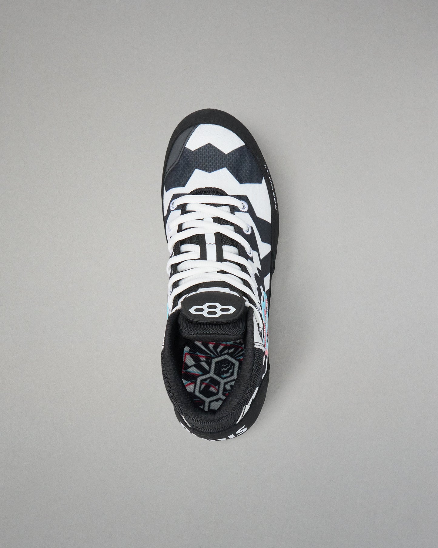 A single high-top wrestling shoe shown from a top-down view on a neutral gray background. The shoe features a black and white geometric pattern on the upper, white laces, and a black collar with a white logo.