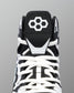 Close-up of a high-top wrestling shoe showing the black tongue with a white geometric logo, white laces, and white contrast overlays on a gray background.