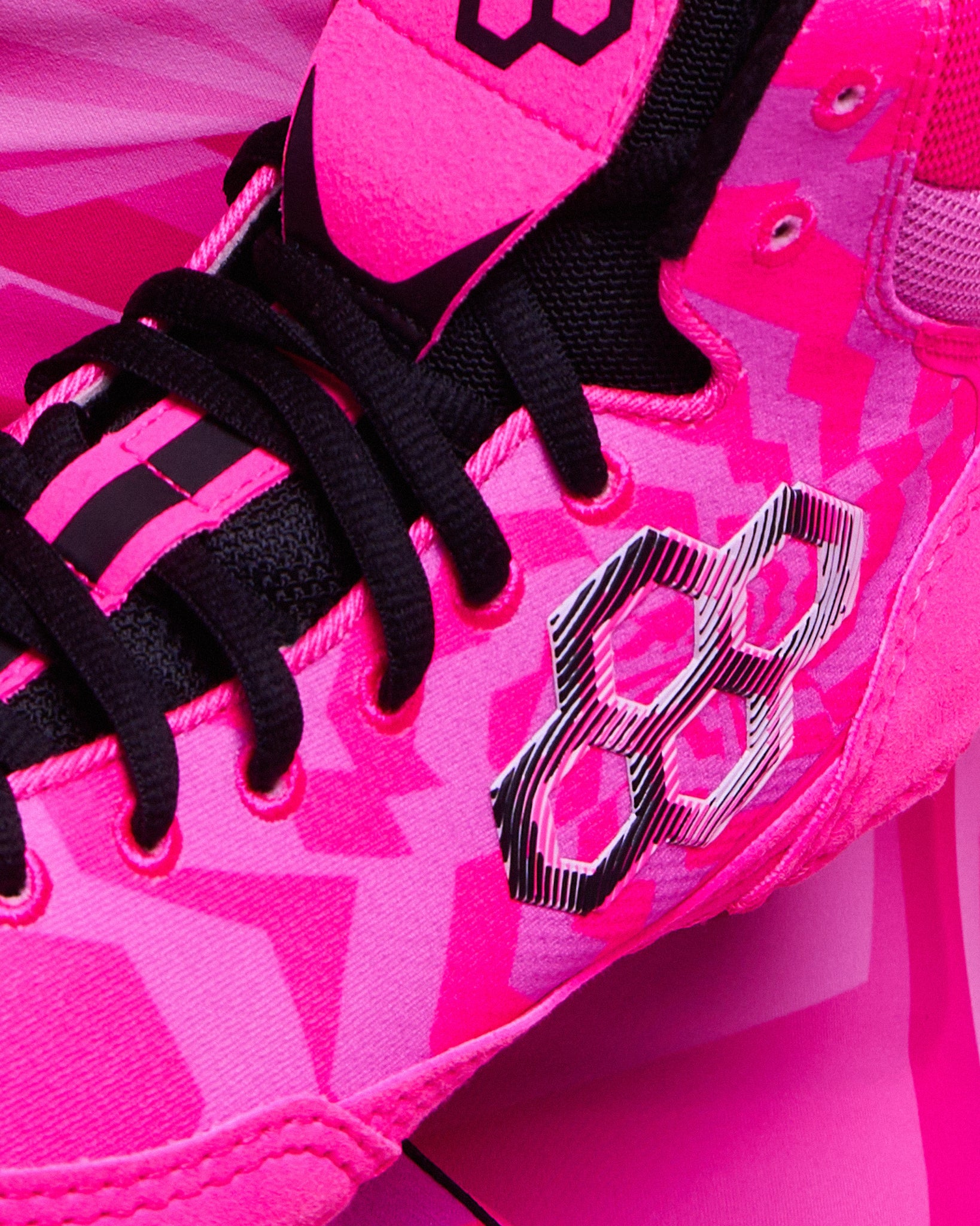 Close-up of a wrestling shoe in bright pink and magenta with black laces and a black geometric logo on the side.