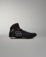 A high-top black Wrestling Shoe with gray geometric side detailing and bright orange accents on the collar, laces, and outsole, shown against a neutral gray background.