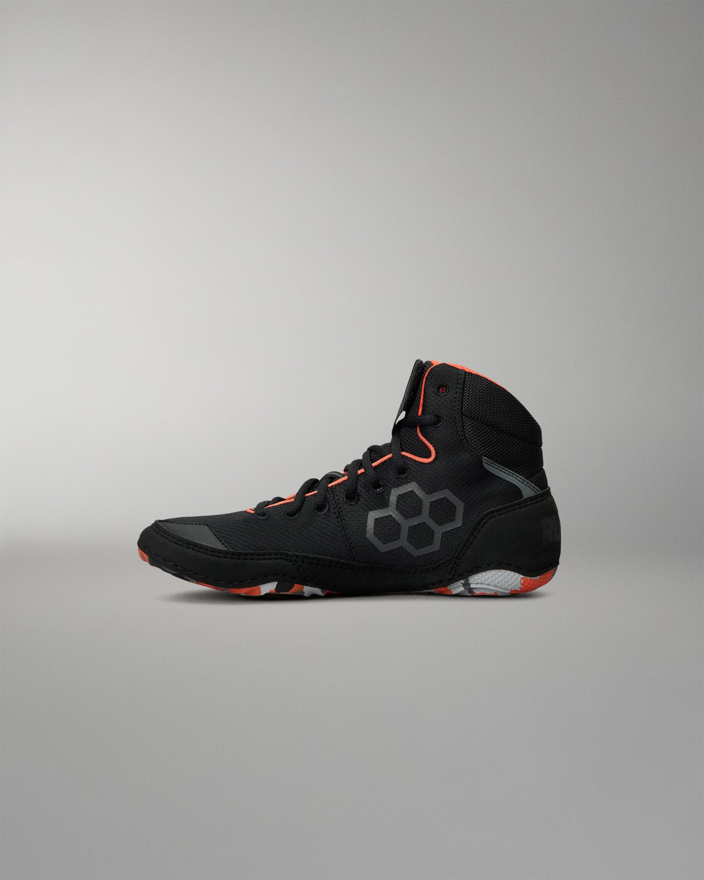 A high-top Wrestling Shoe in black with gray geometric patterns and bright orange accents on the laces, collar lining, and outsole, shown in profile against a neutral gray background.
