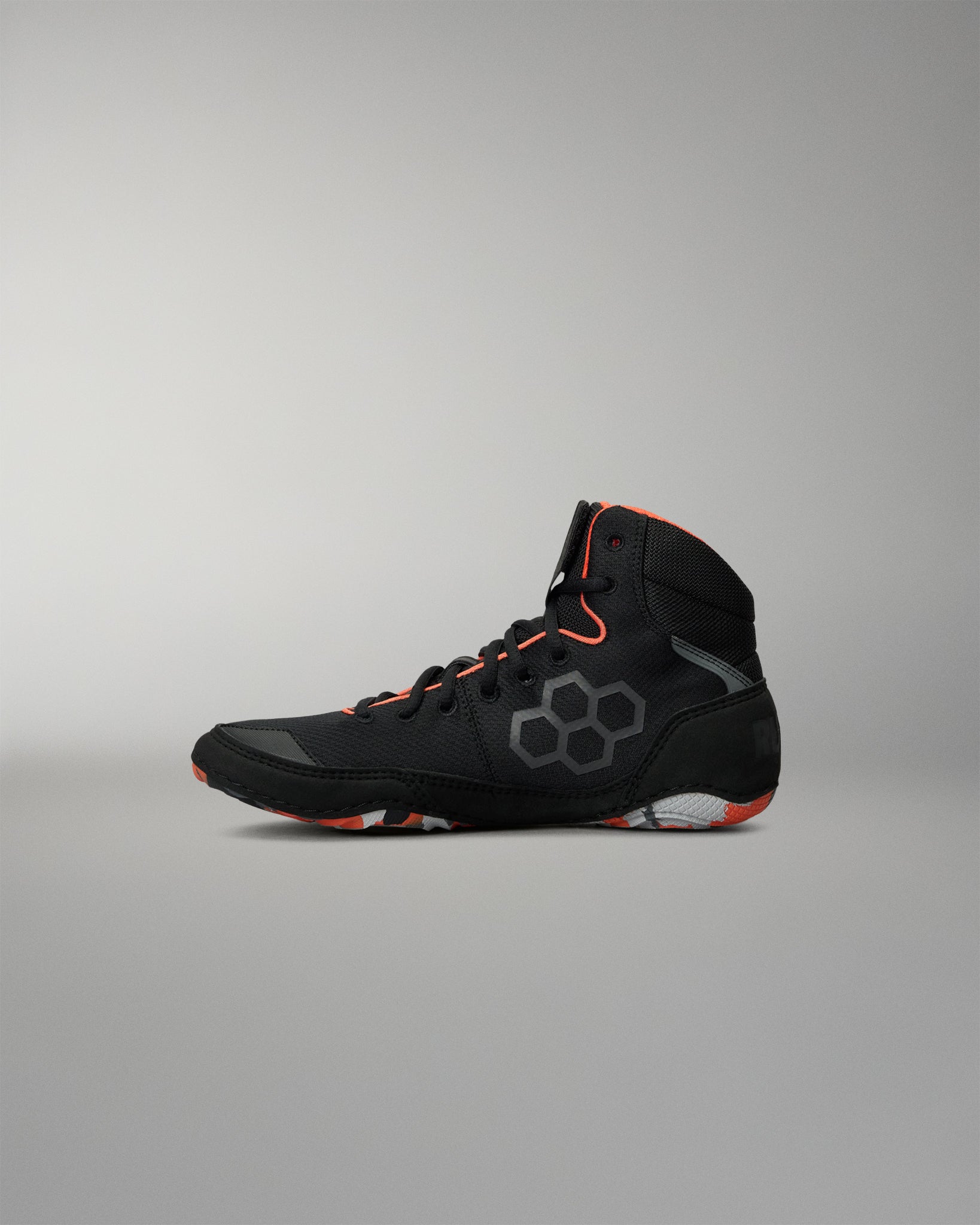 A high-top Wrestling Shoe in black with gray geometric patterns and bright orange accents on the laces, collar lining, and outsole, shown in profile against a neutral gray background.