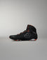 A high-top Wrestling Shoe in black with gray geometric patterns and bright orange accents on the laces, collar lining, and outsole, shown in profile against a neutral gray background.