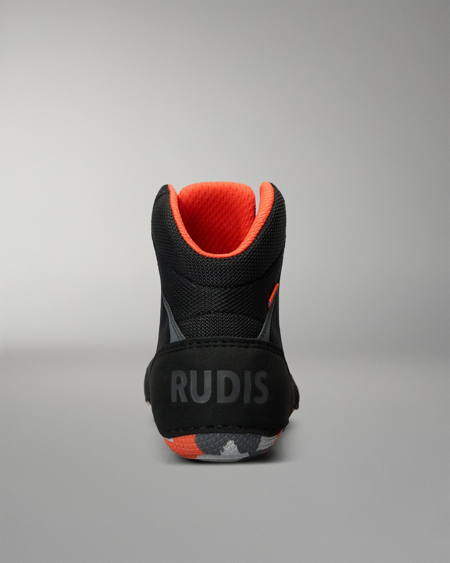 A high-top black Wrestling Shoe shown from the back, featuring a bright orange interior lining, a black sole with 'RUDIS' printed in gray, and orange and gray accents on the outsole.