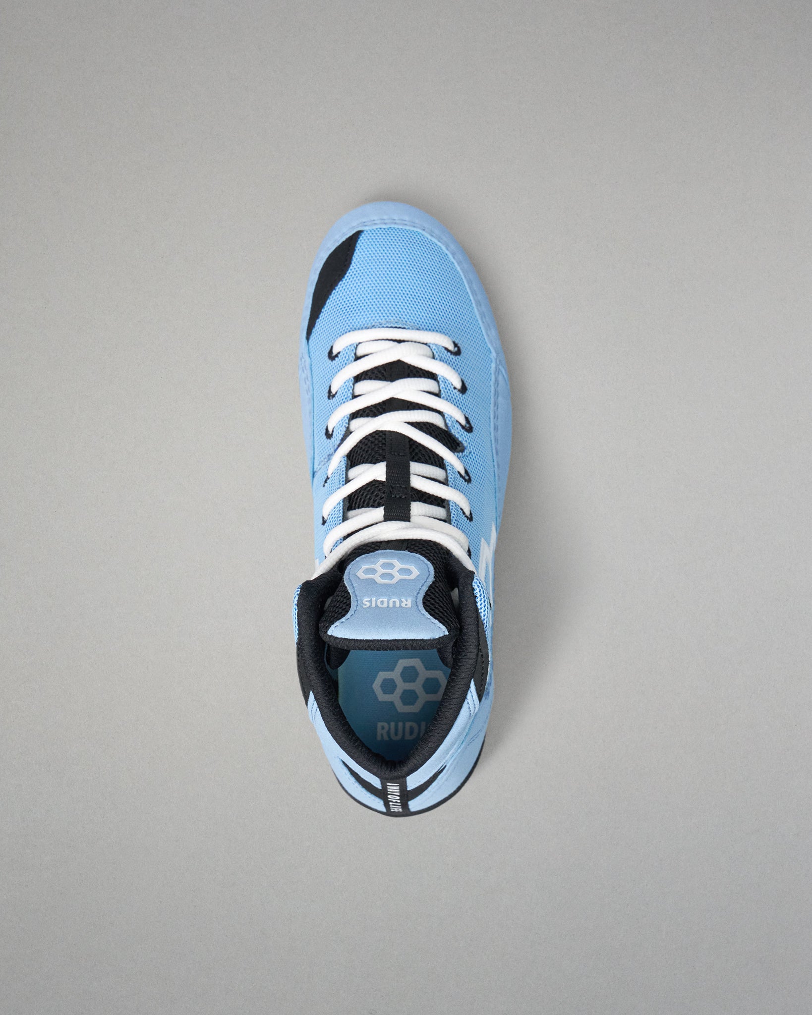 A light blue low-top wrestling shoe with black and white accents, featuring white laces and a visible RUDIS logo on the tongue and heel, photographed from a top-down angle on a neutral gray background.