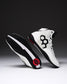 A pair of high-top wrestling shown on a dark gray to black gradient studio background. One shoe is upright showing a white leather upper with a large black geometric side logo, white laces, black trim, and a small red circular detail near the heel.