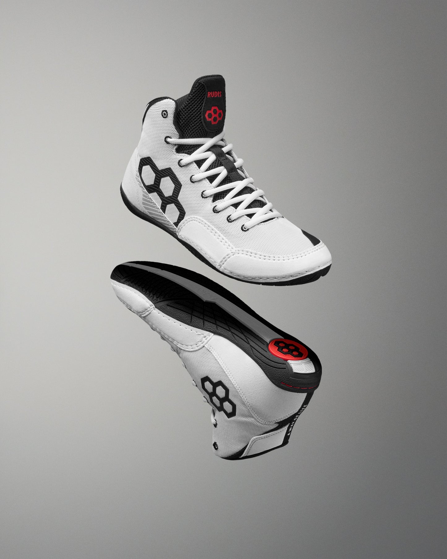 A pair of high-top athletic wrestling shoe shown floating against a smooth gray gradient background. The shoes are primarily white with black panels, black laces, and a small red logo detail on the tongue and heel.