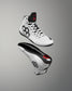 A pair of high-top athletic wrestling shoe shown floating against a smooth gray gradient background. The shoes are primarily white with black panels, black laces, and a small red logo detail on the tongue and heel.