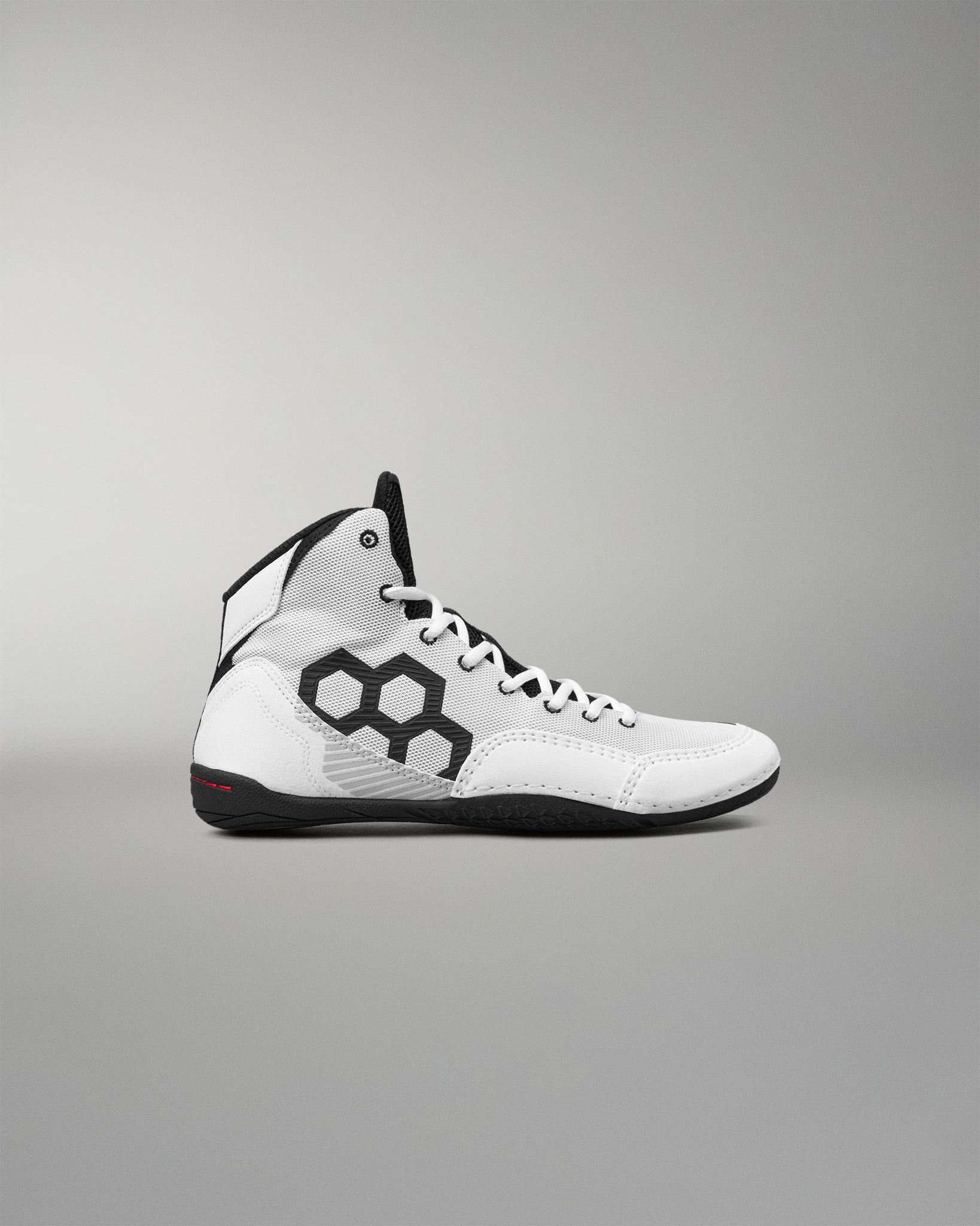 A high-top athletic wrestling shoe in white with black accents, featuring a black hexagonal pattern on the side and a black sole, shown against a neutral gray background.