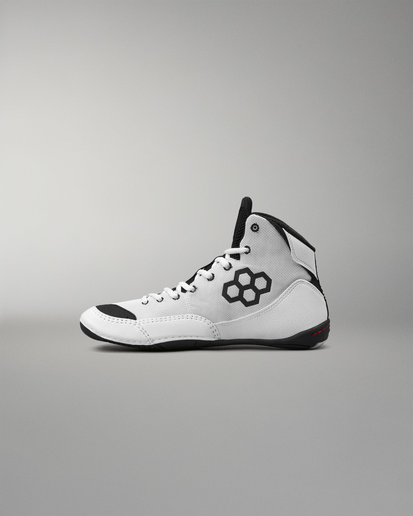 A white high-top wrestling shoe with black accents, including a black geometric logo on the side, black laces, and a black outsole, shown in profile against a neutral gray background.