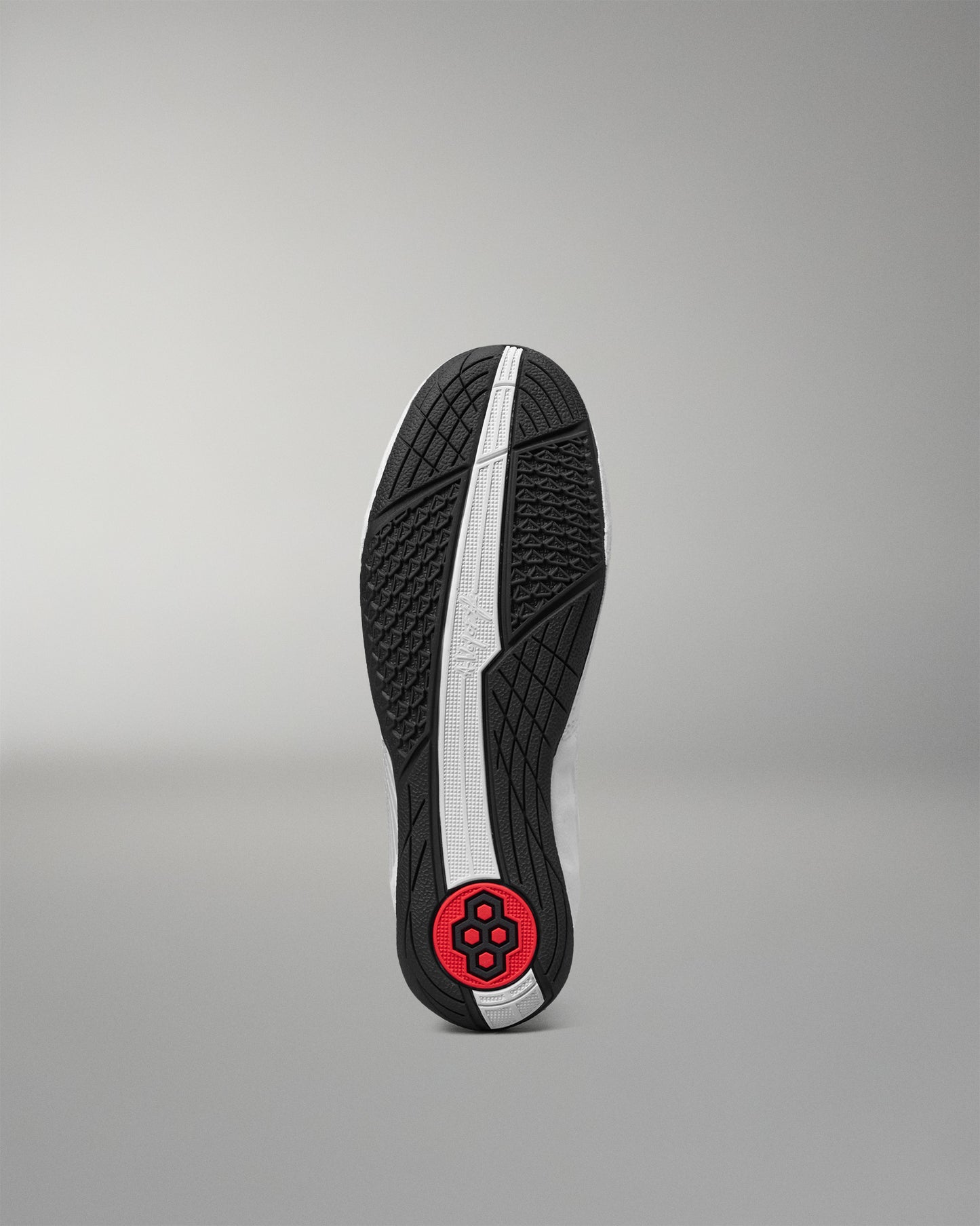 The outsole of a black wrestling shoe is shown vertically against a neutral gray background, featuring a textured black tread pattern, a central white stripe, and a red circular logo near the heel.