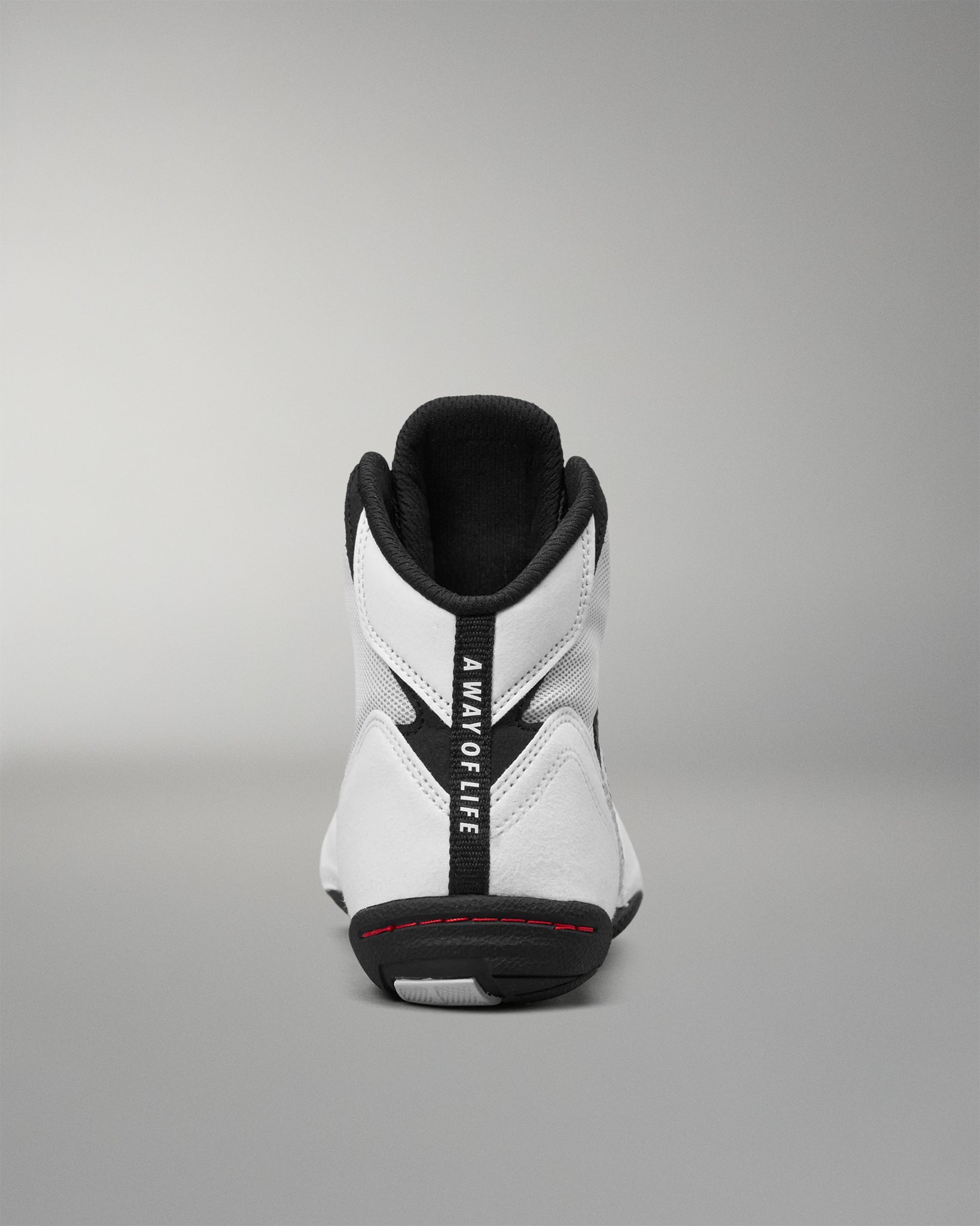 A white high-top wrestling shoe shown from the back, featuring a prominent black vertical strap with the text 'A WAY OF LIFE' in white, a black outsole, and a thin red accent line near the heel.