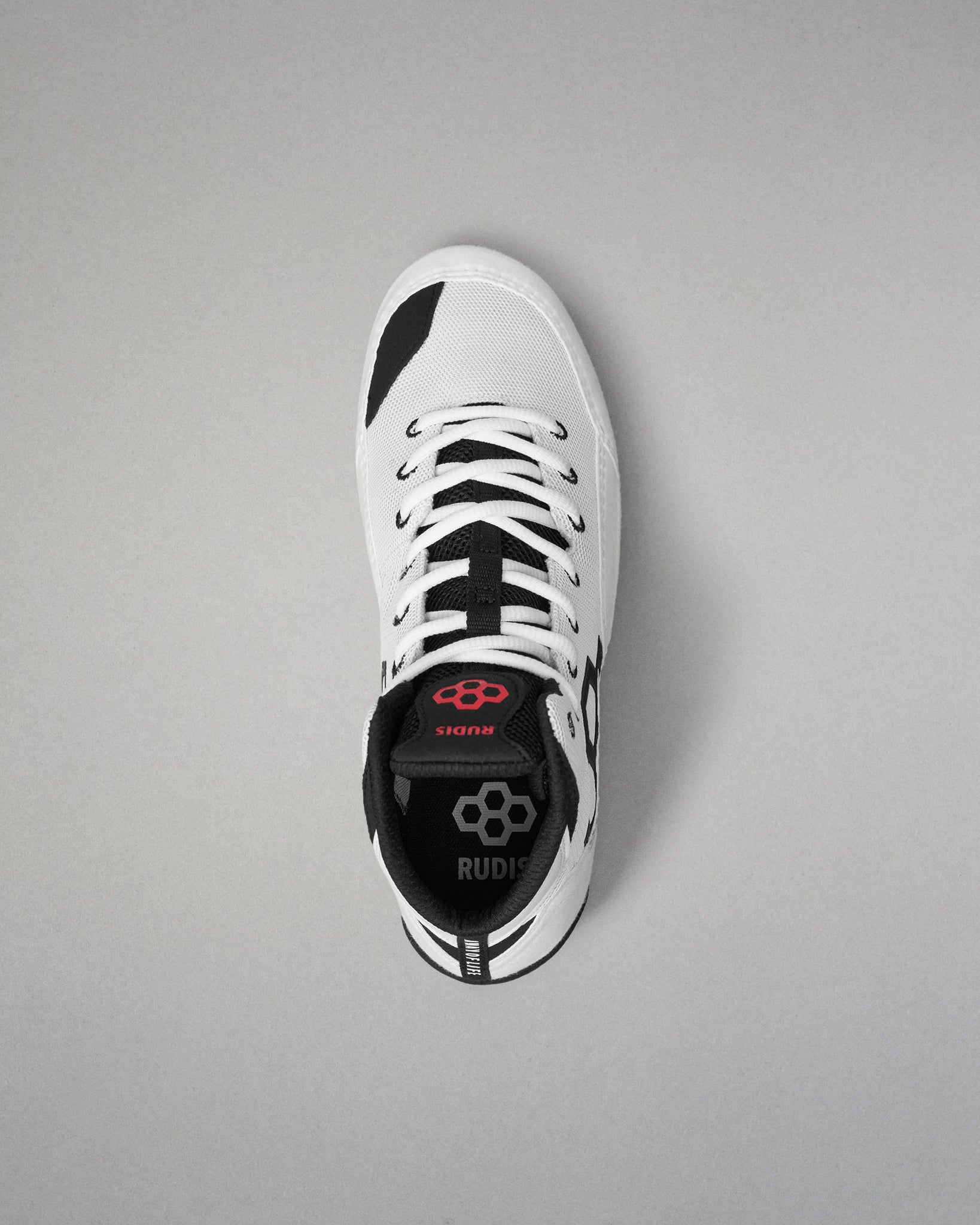 A white low-top wrestling shoe with black accents and white laces, shown from a top-down view on a neutral gray background. The brand name 'RUDIS' is visible on the black heel collar.