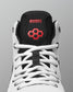 Close-up of a high-top wrestling shoe showing the tongue area, with a white mesh upper, black collar and tongue, white laces, and red embroidered branding that reads RUDIS with a red hexagon logo.