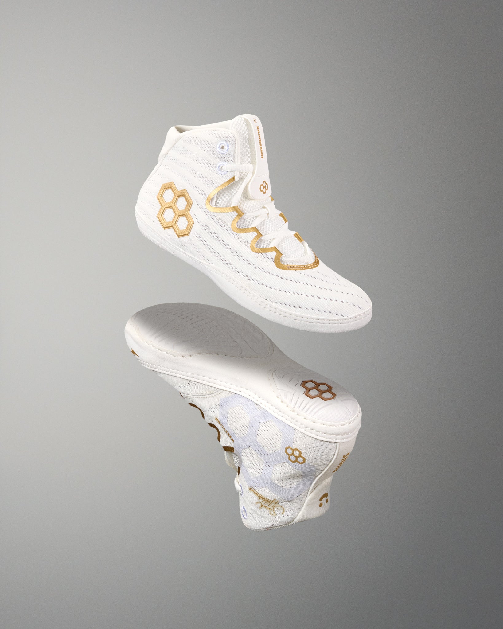 A white high-top athletic wrestling shoes with gold geometric and wavy accents, shown floating above its matching sole on a smooth gray gradient background.