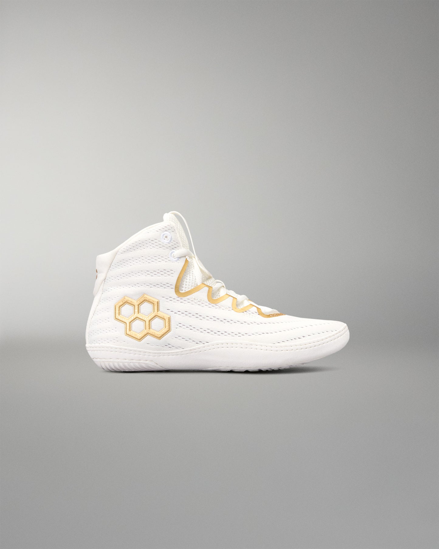 A white high-top athletic wrestling shoe with gold accents, including a gold honeycomb logo on the side and gold embroidered details on the laces, shown against a neutral gray background.