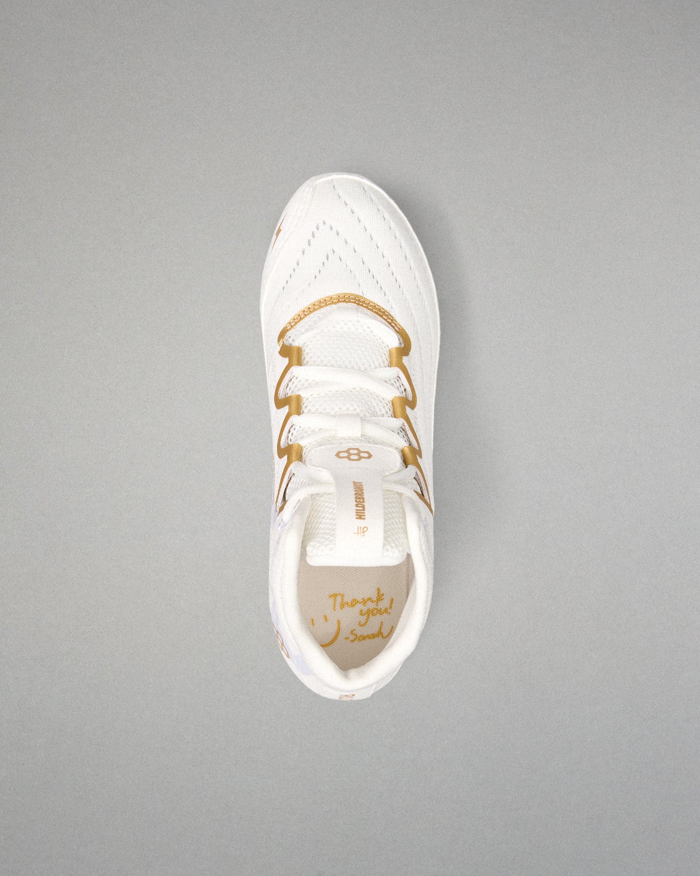 A white athletic wrestling shoe with gold accents and gold laces, shown from a top-down view on a solid gray background.