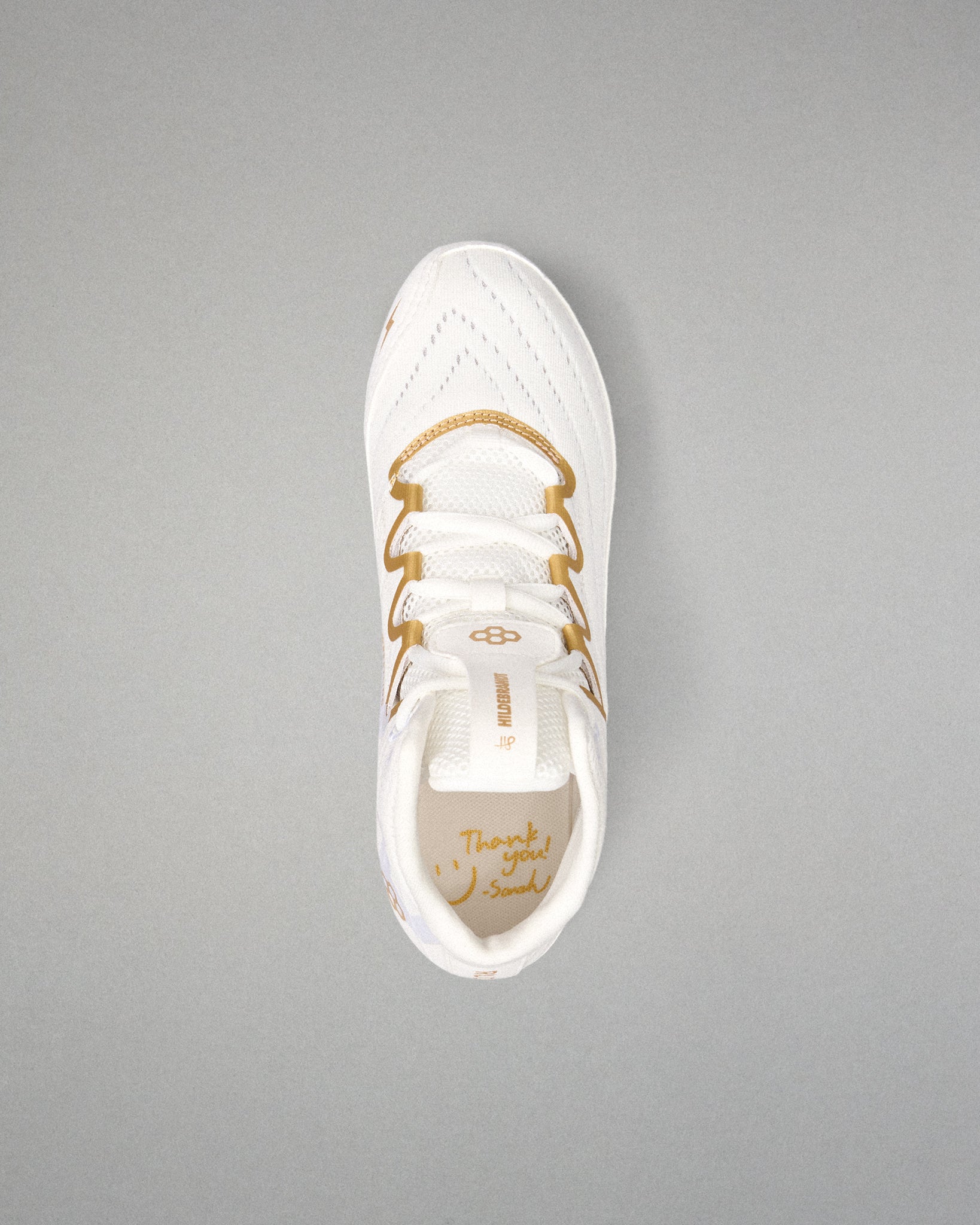 A white athletic wrestling shoe with gold accents and gold laces, shown from a top-down view on a solid gray background.