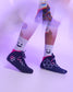 A person wearing dark navy high-top wrestling shoes with pink and gray graphic details, paired with white crew socks featuring a black smiley face, shown against a purple-lit studio background.