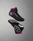 A pair of high-top wrestling shoes floating against a neutral gray gradient background. The shoes are primarily black with vibrant pink accents on the collar and sole, and gray and white geometric hexagonal patterns on the side and heel.