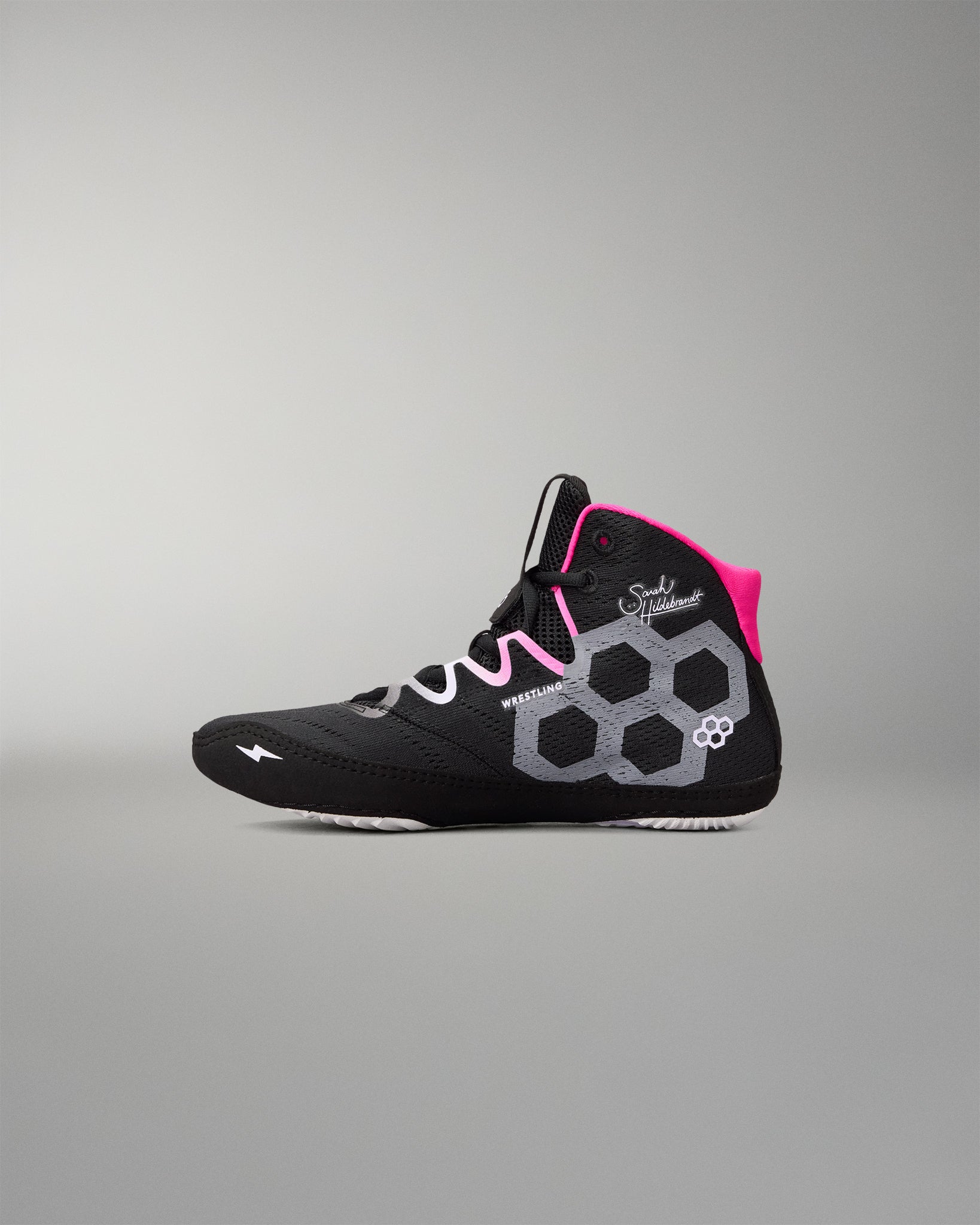 A high-top wrestling shoe in black with a bright pink collar lining, white and gray geometric side patterns, and white laces, shown against a neutral gray background.