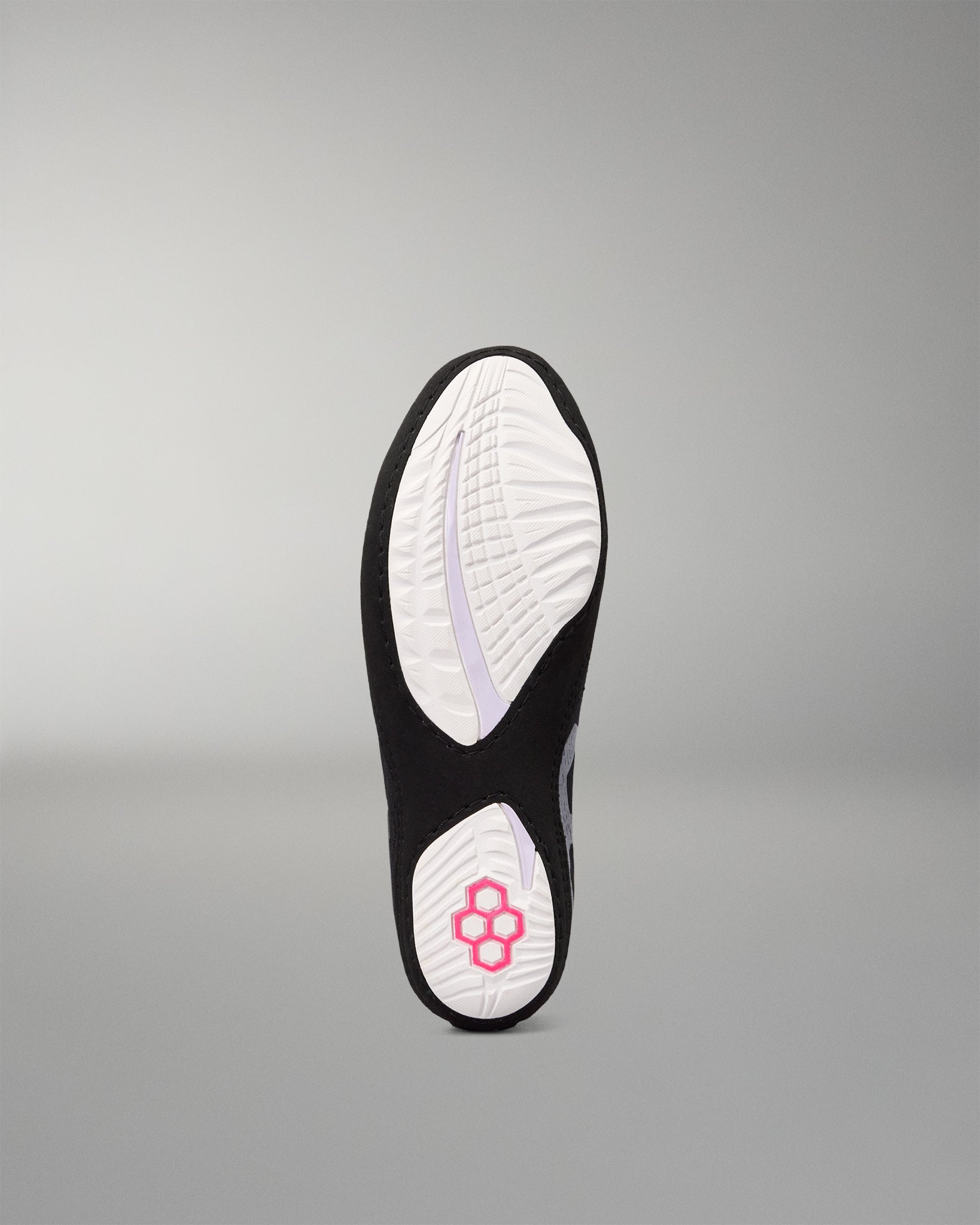 The outsole of a black and white wrestling shoe, featuring a white tread pattern with a pink flower logo on the heel, shown against a neutral gray background.