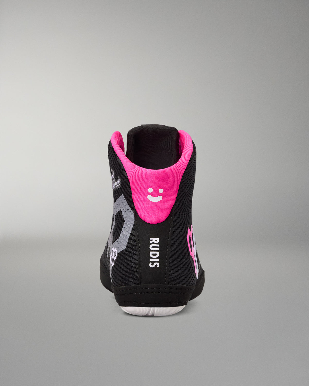 A black high-top wrestling shoe shown from the back, featuring a vibrant hot pink collar with a white smiley face, gray graphic patterns, and the brand name 'RUDIS' printed vertically in white.