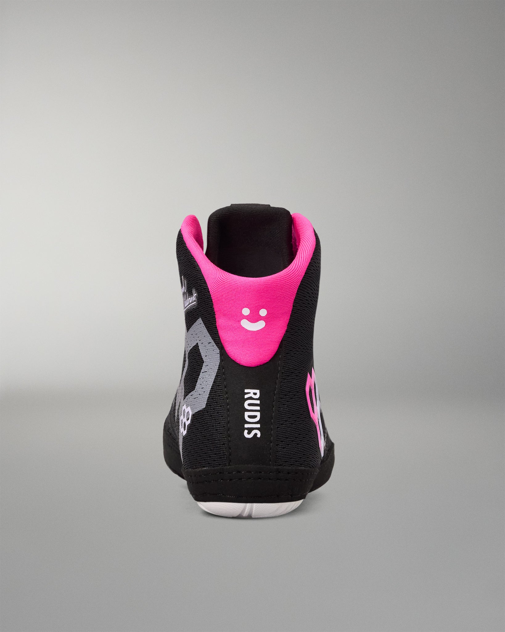 A black high-top wrestling shoe shown from the back, featuring a vibrant hot pink collar with a white smiley face, gray graphic patterns, and the brand name 'RUDIS' printed vertically in white.