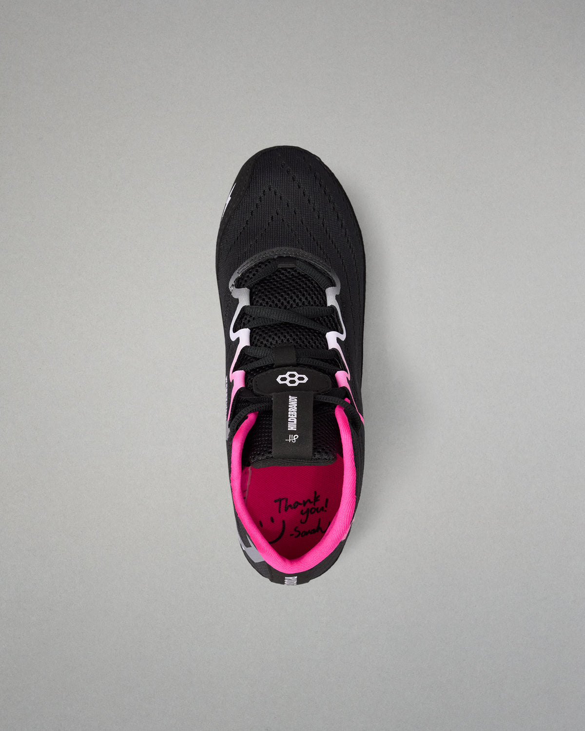 A black wrestling shoe with bright pink lining and white laces, shown from a top-down view on a neutral gray background.