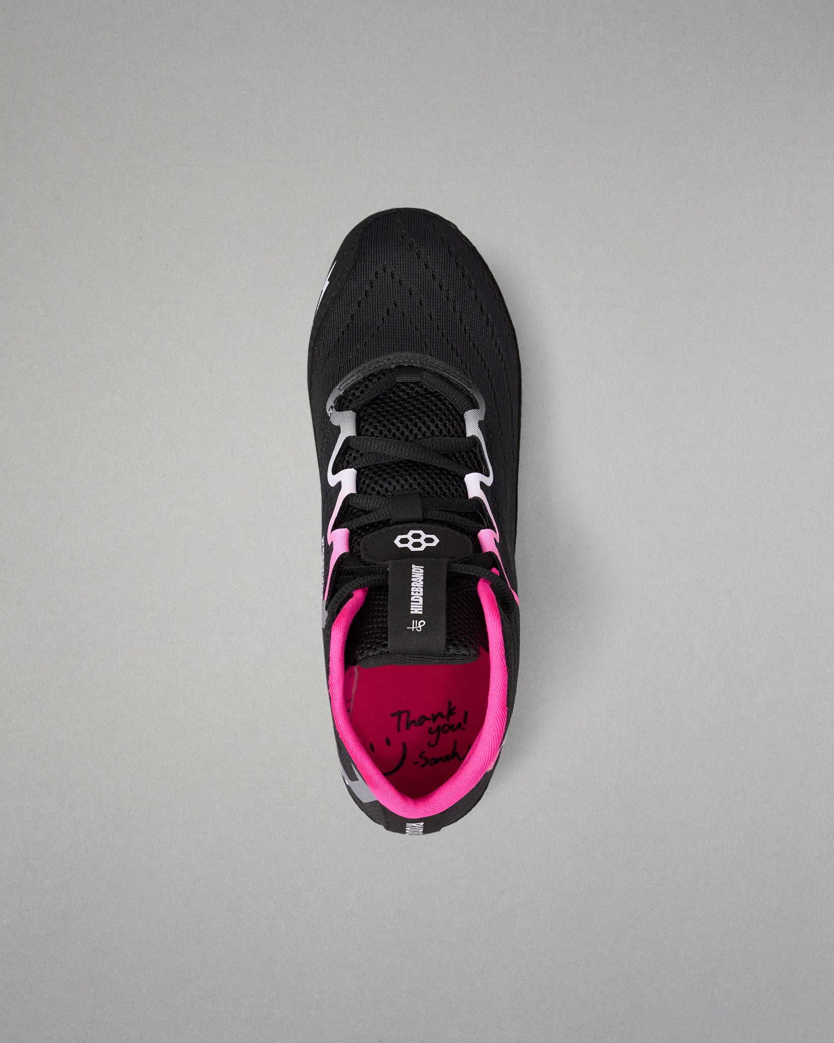 A black wrestling shoe with bright pink lining and white laces, shown from a top-down view on a neutral gray background.