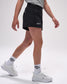 Person wearing black shorts with a logo, white sneakers, and socks on a light gray background