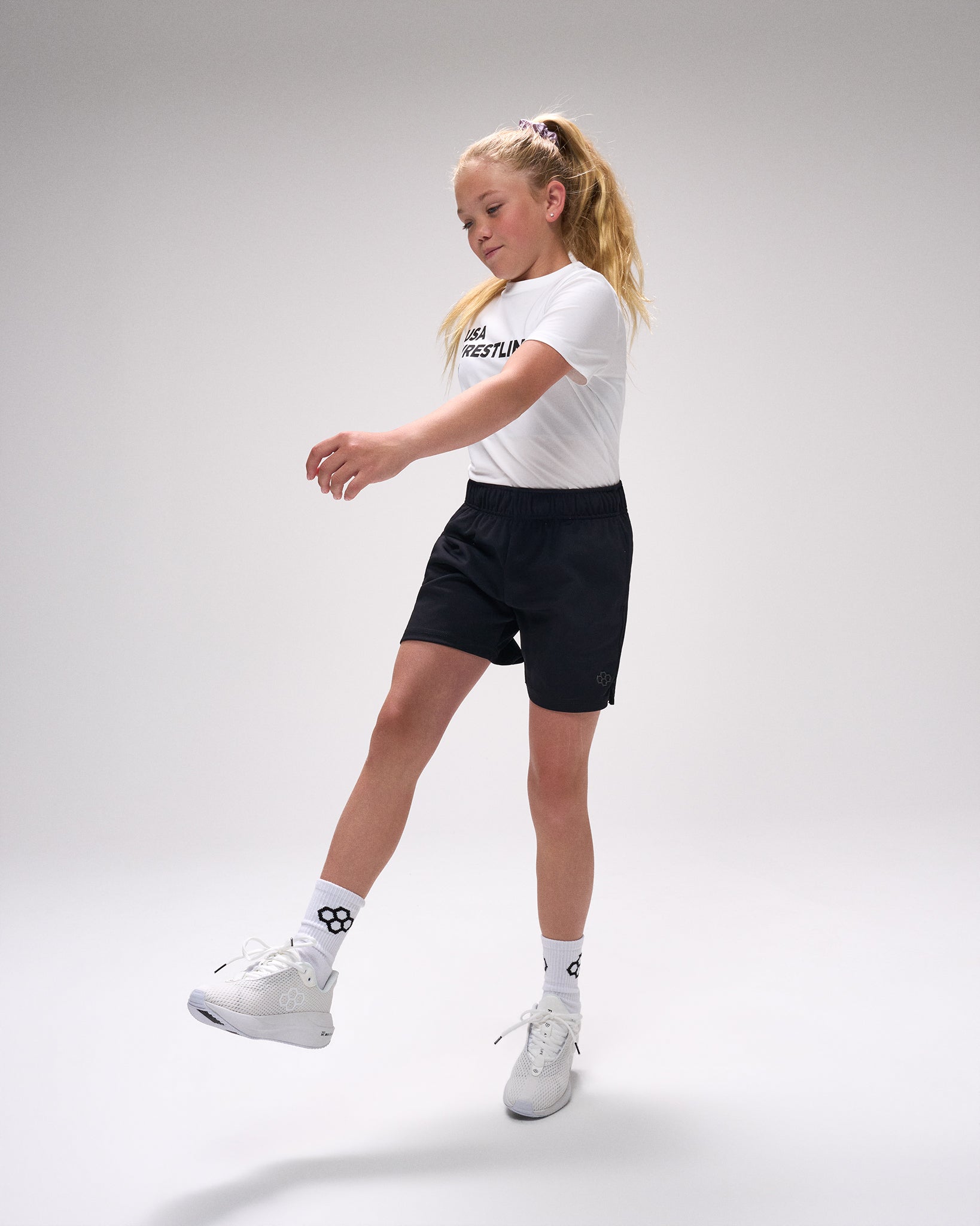 Young girl in a white t-shirt and black shorts standing on a light gray background