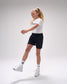 Young girl in a white t-shirt and black shorts standing on a light gray background