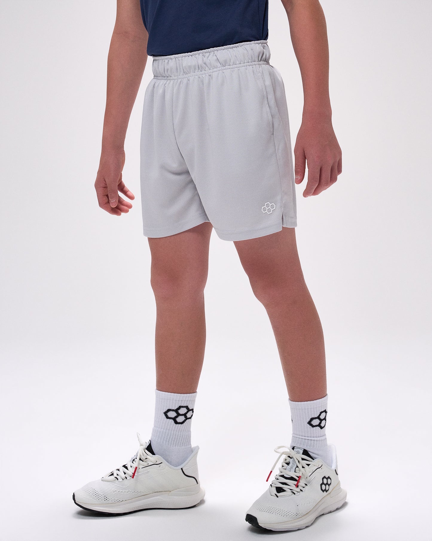 Person wearing light gray shorts, white socks with a logo, and white sneakers on a white background