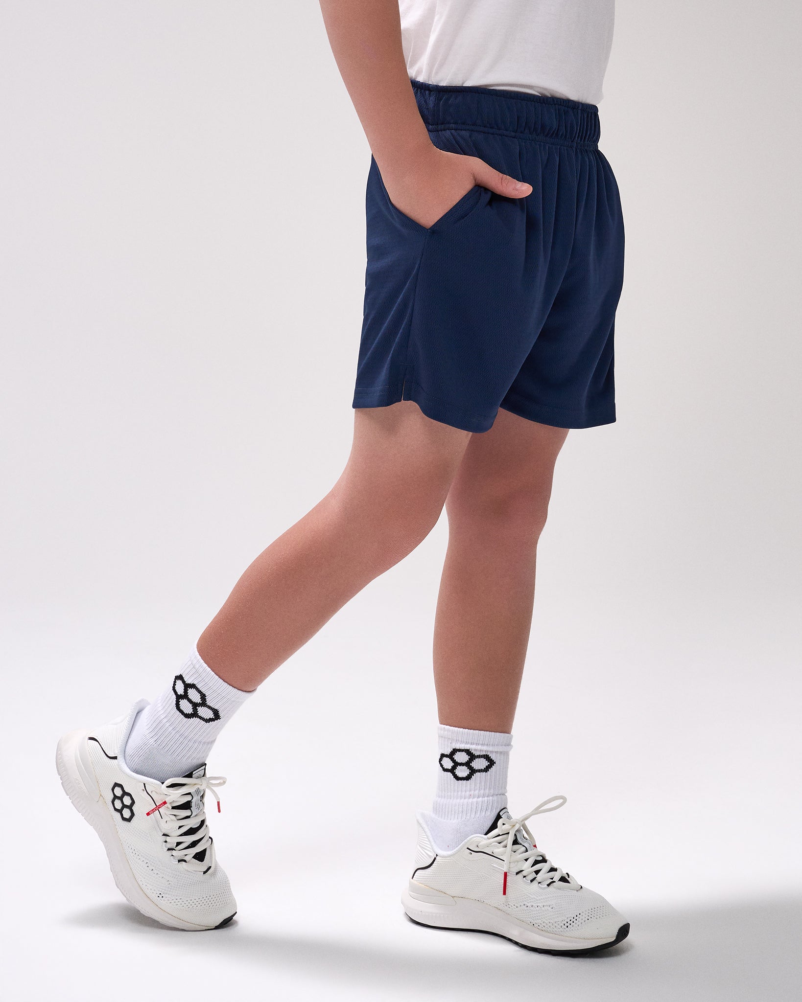 Person wearing navy shorts and white sneakers on a plain background