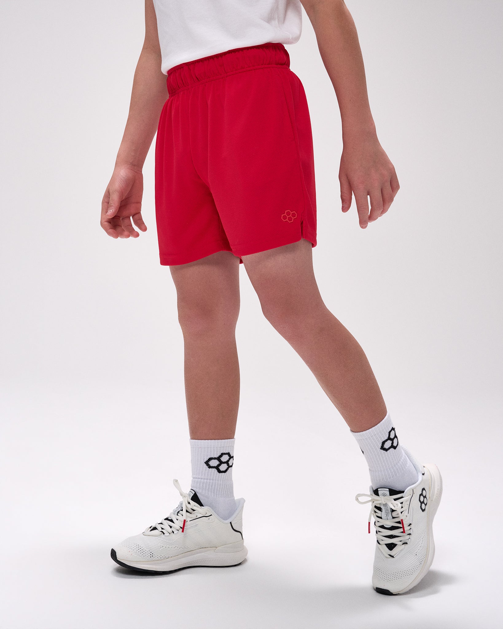 Person wearing red shorts, white socks with a logo, and white sneakers on a light gray background