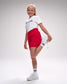 Young girl in white t-shirt with 'Wrestling' text, red shorts, and white sneakers on a gray background