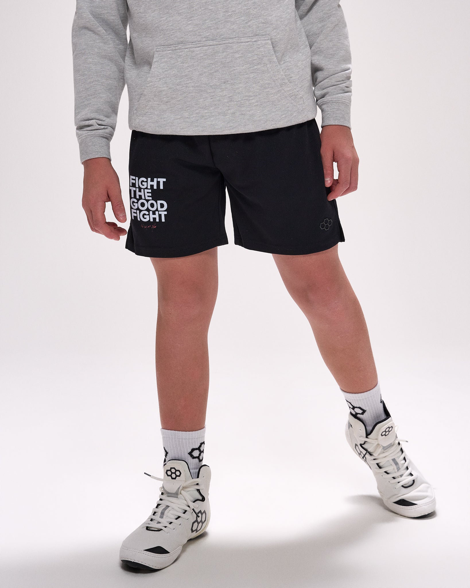 Person wearing black shorts with text and white sneakers on a light gray background