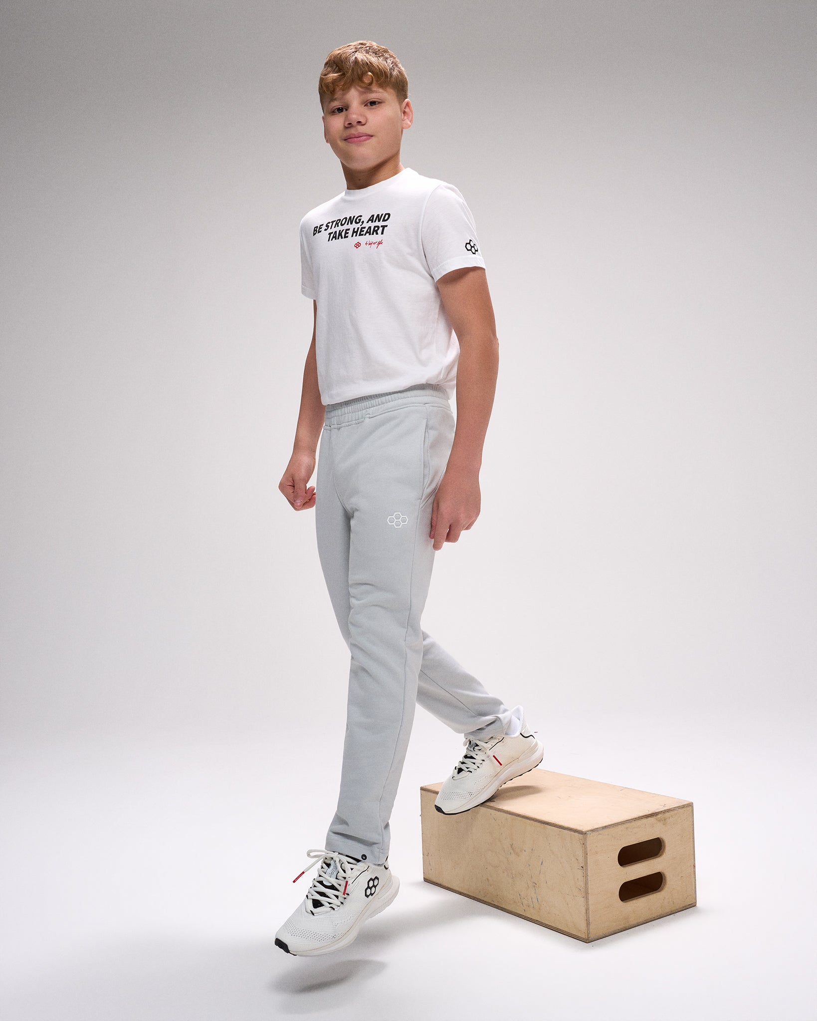Person wearing a white t-shirt and gray pants standing on a wooden box against a plain background