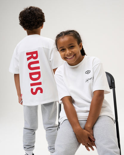 Two youth athletes model the white RUDIS Script Youth Drop Shoulder Tee with gray joggers, showcasing the red vertical RUDIS back graphic.