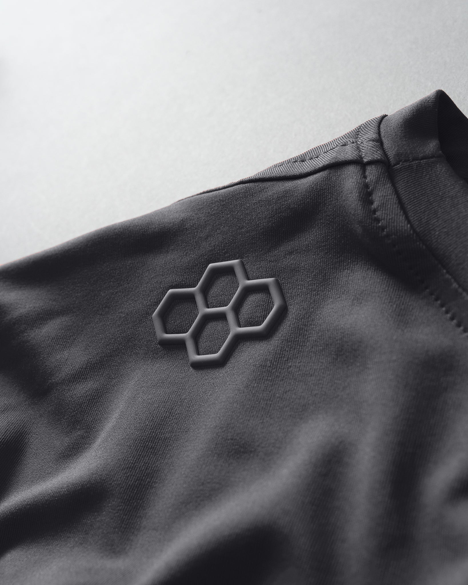 Close-up of a dark fabric with a geometric logo on a light gray background