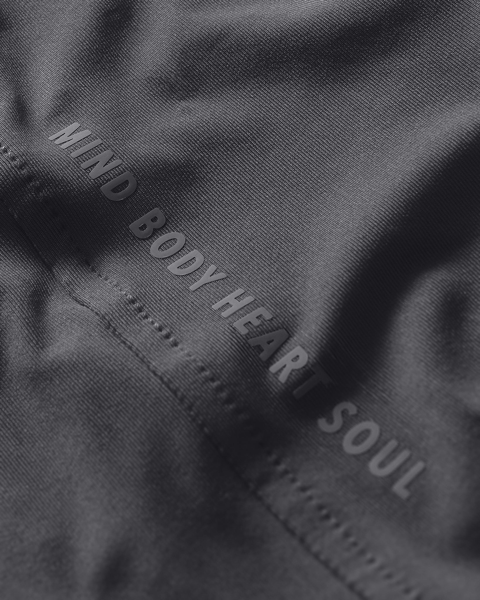 Text 'MIND BODY HEART SOUL' embroidered on a dark fabric background