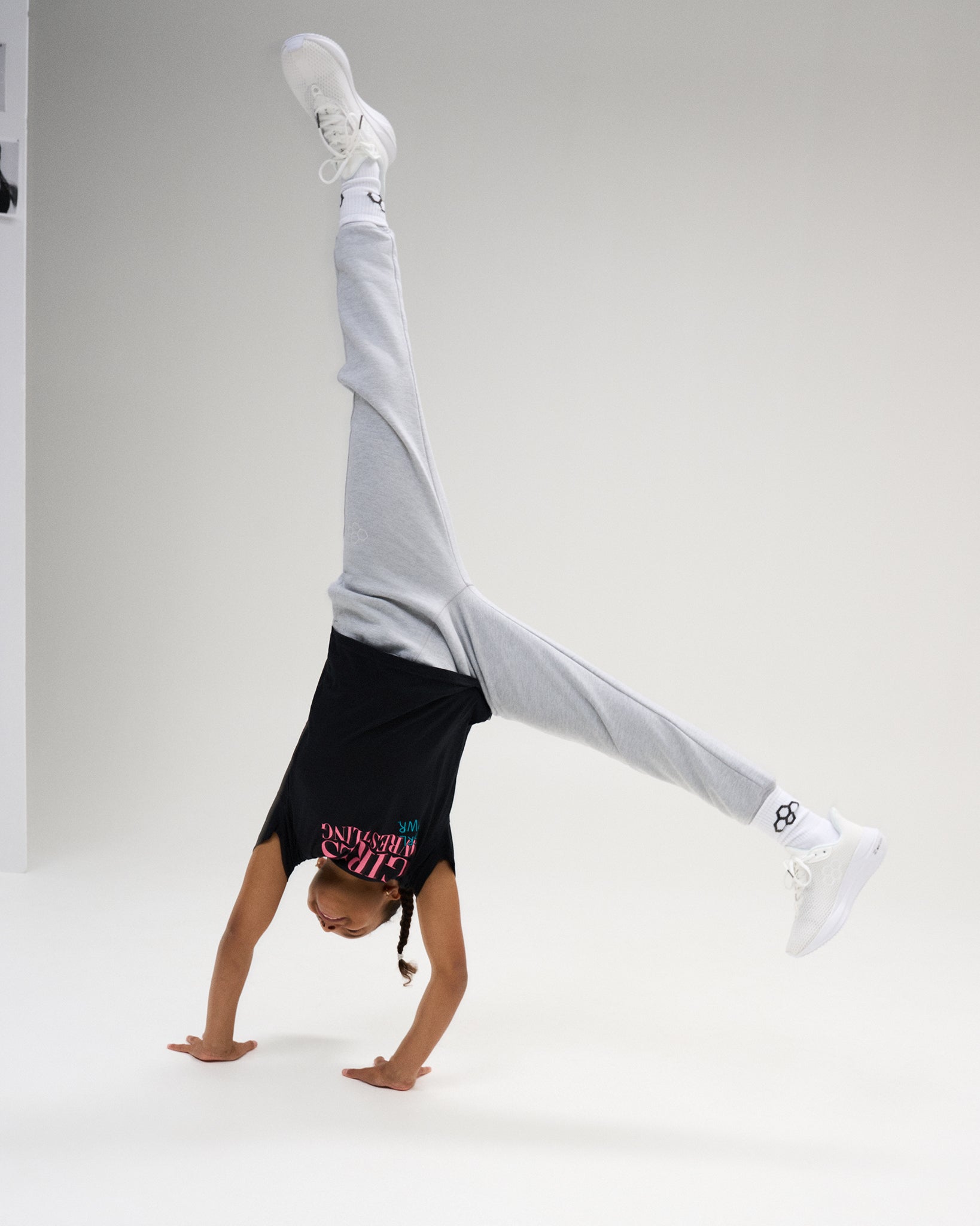 Youth athlete performs a handstand in the black RUDIS Girl Power Wrestling Youth Elite Super Soft T-Shirt with gray joggers and white shoes.